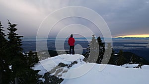 Adventurous Man Hiker on Snowy Mountain with Trees. Cloudy Sunset Sky. British Columbia, Canada