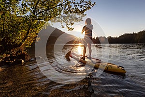 Adventurous Woman Paddling on a Paddle Board in a peaceful lake.