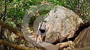 Adventurous woman scales Pidurangala Rock. Solo traveler hikes through dense foliage, navigates large boulders in Sri