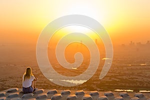 Adventurous woman sitting on top of skyscraper overlooking the city at sunrise