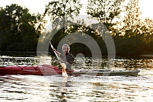 Adventurous young caucasian guy holding a paddle while boating on a lake surrounded by peaceful nature at sunset
