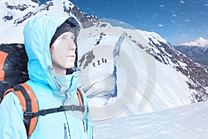 Adventurous young man with backpack standing on mountain top view and looking out. Snowboarders walking uphill for