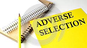 ADVERSE SELECTION text written on a yellow paper with notebook