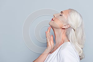 Advertisement concept. Close up profile with copy space of nice, charming, aged woman, touching her skin of neck with hand over g
