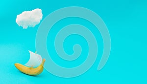 Advertisement idea with a cloud, yellow banana like a ship and a sail of paper against pastel blue background. Minimal summer