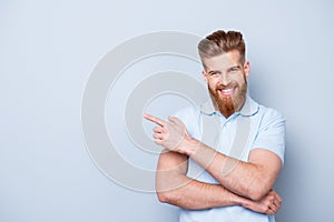 Advertising barber shop concept. Young handsome red bearded stylish guy is pointing on a copyspace on pure light background