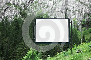 Advertising billboard with empty white mockup in green forest of mountains.