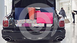 An advertising car stands in a shopping center. The open trunk of a car is full of shopping bags.