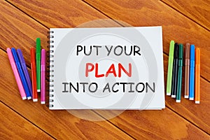 Advice and motivation. Top view of colorful pen and notebook written with Put Your Plan Into Action on wooden background.