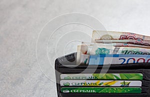 Russian banknotes in denominations of 1000, 2000 and 5000 rubles and credit cards Sberbank in a black leather purse close-up, on a