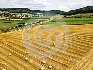 Aeiral view of farming field with hay bale rolls and a train is passing by