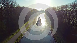 Aerial 4K Bird view shot with a drone of waterway with a barge or freight cargo ship sailing across the natural green