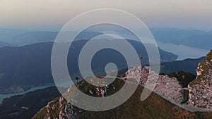 Aerial 4k orbital drone sunset at mountain peak with cross. Hiker girl climbing and taking pictures