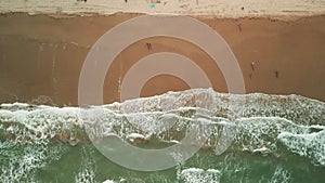 Aerial above shot of sand beach on a summer day while turquiose sea waves breaking on coastline. Top view