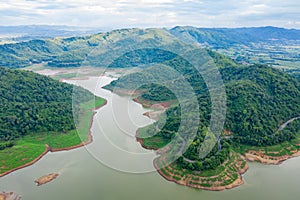 Aerial above view green mountain forest and dam reservoir river in the rain season and curved road on the hill connecting