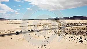 Aerial above view of yellow tropical sandy beach with black long way road and car traveling - ocean blue waves and shore - sunset