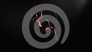 Aerial acrobat in the air ring. Young woman performs the acrobatic elements in the air hoop. Aerialist in on black