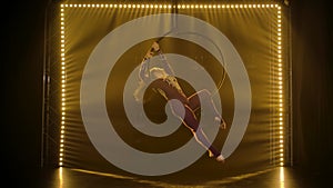 Aerial acrobat in the ring. A young girl performs the acrobatic elements in the air ring. Shot in a dark studio with