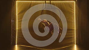 Aerial acrobat in the ring. A young woman performs the acrobatic elements in the air ring surrounded by soft yellow