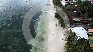 Aerial of Alona beach with blue water, green palm trees, boats and people, Bohol Island, Philippines