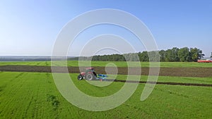 Aerial arc shot of red tractor working on green field plowing soil