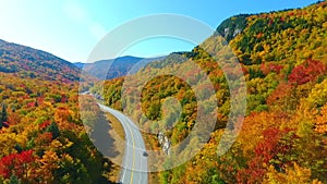 Aerial backwards over stunning road through New Hampshire mountains during peak fall foliage