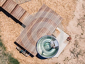 Aerial bird`s eye drone view of a wood fired stainless steel outdoor jacuzzi and a wooden deck with stairs photo
