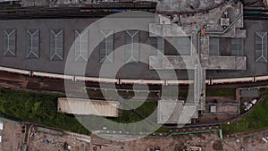 Aerial birds eye overhead top down ascending footage of White City train station. Flat roof with lightboxes. London, UK