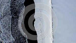 Aerial: birdsview of black beach with white arctic snow in Iceland in winter snow, ice, waves, water