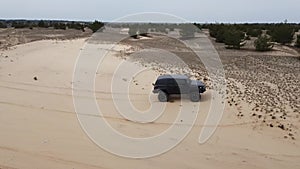 Aerial. Black SUV rides on a sandy road. Side view