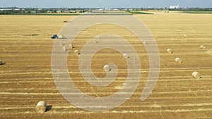 Aerial circling view of tractor tow trailed bale machine to collect straw from harvested field