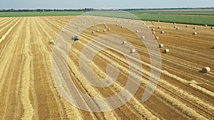 Aerial circling view of tractor tow trailed bale machine to collect straw from harvested field