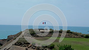 Aerial circular shot of the flag of France on a flagpole on a cliff