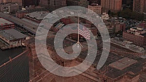 AERIAL: Close up circle flight over Brooklyn Bridge with american flag and East River view Manhattan New York City