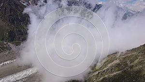 Aerial: Cloudy mountain gorge with glacier at sunny day