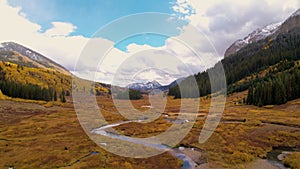 Aerial Colorado Wilderness Epic Landscape in Autumn. Streams wind through valley flying towards mountain snow peak on a cloudy