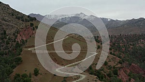 An aerial of cyclists climbing switchbacks towards a ridge of snowy peaks.