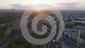 Aerial descending footage of complex of modern buildings in city against sunset. Train passing around on railway tracks