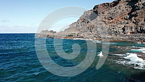 Aerial dolly over Atlantic ocean coast with volcanic relief in sunny