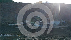 Aerial dolly over lava to village against the sun with rays in frame