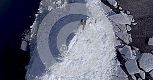 Aerial dron view of young active happy man staying on the ice glaciers near coastline of winter sea. Drone view.