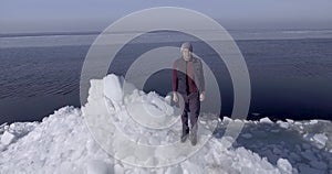 Aerial dron view of young active happy man staying on the ice glaciers near coastline of winter sea. Drone view.