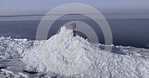 Aerial dron view of young active happy man staying on the ice glaciers near coastline of winter sea shaking hand. Drone