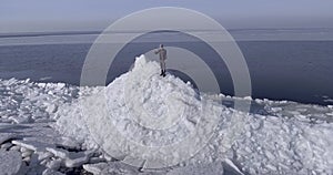 Aerial dron view of young active happy man staying on the ice glaciers near coastline of winter sea weaving hand.