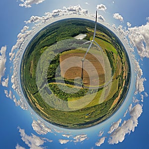 Aerial drone 360 degree view on wind turbine, snake shape road, wheat fields and forest during summer