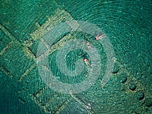 Aerial drone bird`s eye view photo of tourists snorkeling above old Sunken City of Epidauros, Greece