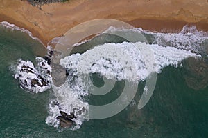 Aerial drone bird view shot of the sea shore with turquoise blue water, large white waves and foam, empty beach with yellow sand,