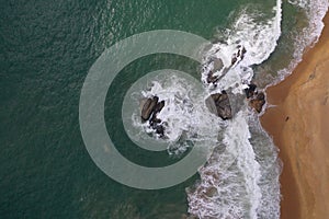 Aerial drone bird view shot of the sea shore with turquoise blue water, large white waves and foam, empty beach with yellow sand,