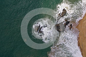 Aerial drone bird view shot of the sea shore with turquoise blue water, large white waves and foam, empty beach with yellow sand,