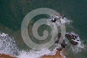 Aerial drone bird view shot of the sea shore with turquoise blue water, large white waves and foam, empty beach with yellow sand,